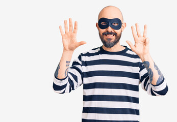 Young handsome man wearing burglar mask showing and pointing up with fingers number nine while smiling confident and happy.