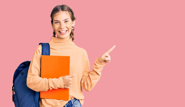 Beautiful caucasian woman with blonde hair wearing student backpack and holding book smiling happy pointing with hand and finger to the side