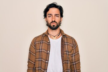 Young handsome hispanic bohemian man wearing hippie style standing over isolated background with serious expression on face. Simple and natural looking at the camera.