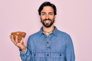 Young handsome hispanic man with bear holding natural ingredient healthy almonds with a happy face standing and smiling with a confident smile showing teeth