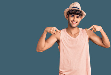 Young hispanic man wearing summer hat looking confident with smile on face, pointing oneself with...