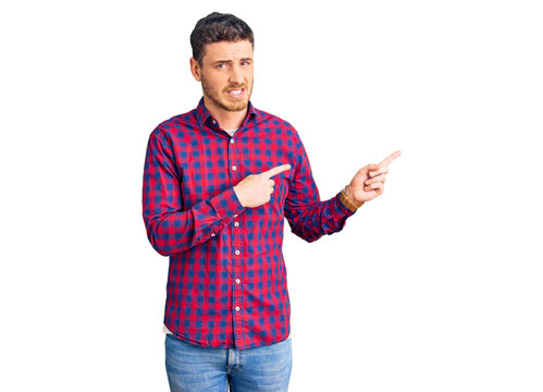 Handsome young man with bear wearing casual shirt pointing aside worried and nervous with both hands, concerned and surprised expression