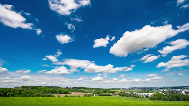 White clouds on blue sky over green field of days time lapse