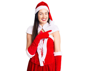 Young beautiful caucasian woman wearing santa claus costume cheerful with a smile on face pointing with hand and finger up to the side with happy and natural expression