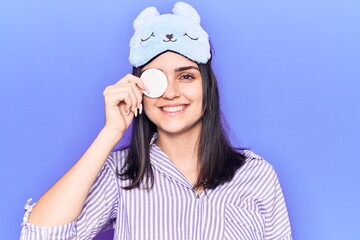 Young beautiful girl wearing funny sleep mask using makeup remover cotton looking positive and happy standing and smiling with a confident smile showing teeth