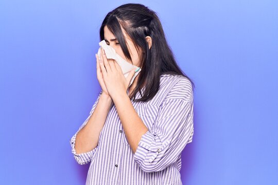 Young hispanic woman illness using paper handkerchief on nose. Standing over isoltated purple background