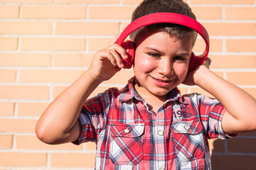 portrait kid listening to music with headphones on brick wall