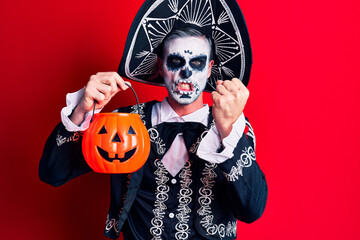 Young man wearing mexican day of the dead costume holding pumpkin annoyed and frustrated shouting with anger, yelling crazy with anger and hand raised