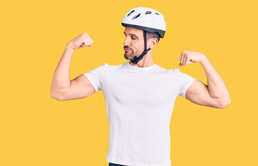 Young handsome man wearing bike helmet showing arms muscles smiling proud. fitness concept.