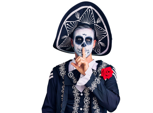 Young man wearing day of the dead costume over background asking to be quiet with finger on lips. silence and secret concept.