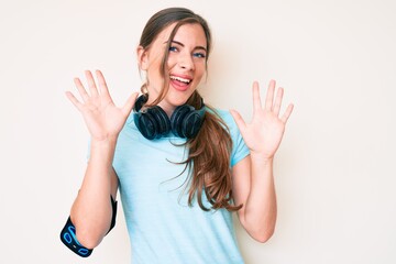 Beautiful young caucasian woman wearing gym clothes and using headphones showing and pointing up with fingers number ten while smiling confident and happy.