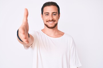 Fototapeta premium Young handsome man wearing casual white tshirt smiling friendly offering handshake as greeting and welcoming. successful business.