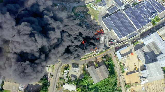 Aerial, top down above firefighters trying to quell the fire, in front of a building on fire, a huge black smoke cloud, in Haina, San Cristobal, Dominican Republic - screwdriver, drone shot