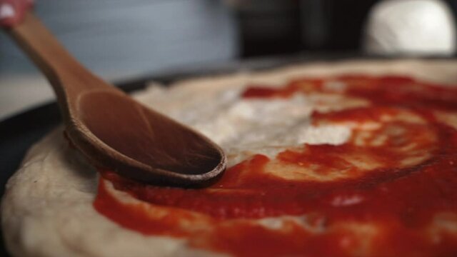 Slow Motion Wooden Spoon Spreading Red Sauce On Pizza Crust. 