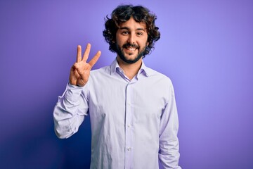 Naklejka premium Young handsome business man with beard wearing shirt standing over purple background showing and pointing up with fingers number three while smiling confident and happy.