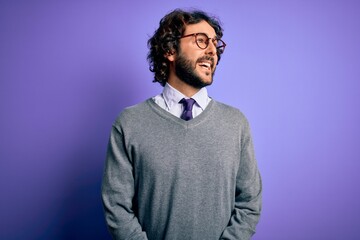 Obraz premium Handsome businessman with beard wearing tie and glasses standing over purple background looking away to side with smile on face, natural expression. Laughing confident.