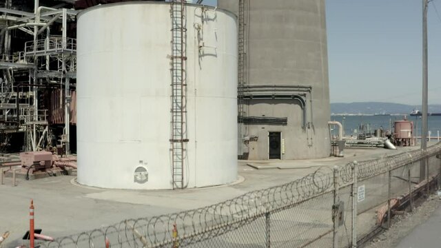 Drone shot moving slowly straight up along over 100 foot tall concrete smokestack with San Francisco bay and blue sky background, attached ladder to top of smokestack, tilts down at top of climb