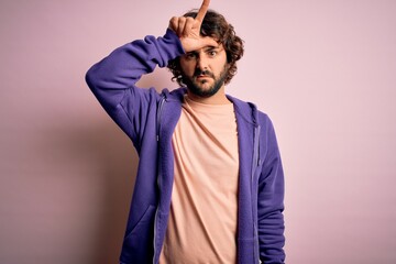 Young handsome sporty man with beard wearing casual sweatshirt over pink background making fun of...