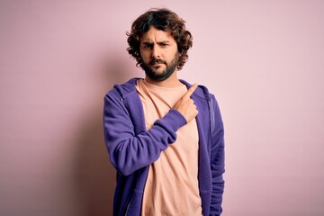Young handsome sporty man with beard wearing casual sweatshirt over pink background Pointing with hand finger to the side showing advertisement, serious and calm face
