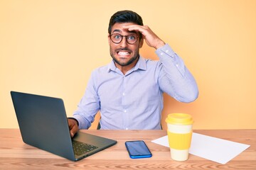 Young hispanic man working at the office drinking a cup of coffee stressed and frustrated with hand on head, surprised and angry face