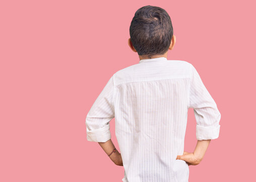 Cute blond kid wearing elegant shirt standing backwards looking away with arms on body