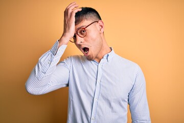 Young handsome hispanic business man wearing nerd glasses over yellow background surprised with...