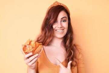 Young beautiful woman holding nachos potato chips smiling happy pointing with hand and finger