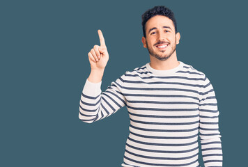 Fototapeta premium Young hispanic man wearing casual clothes pointing finger up with successful idea. exited and happy. number one.