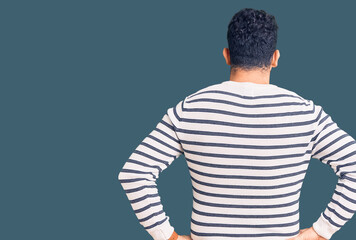 Young hispanic man wearing casual clothes standing backwards looking away with arms on body