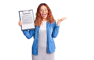 Young latin woman holding clipboard with agreement document celebrating victory with happy smile...
