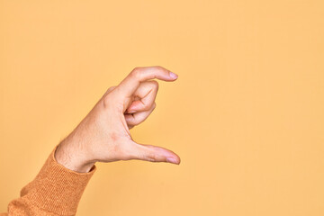 Hand of caucasian young man showing fingers over isolated yellow background picking and taking invisible thing, holding object with fingers showing space