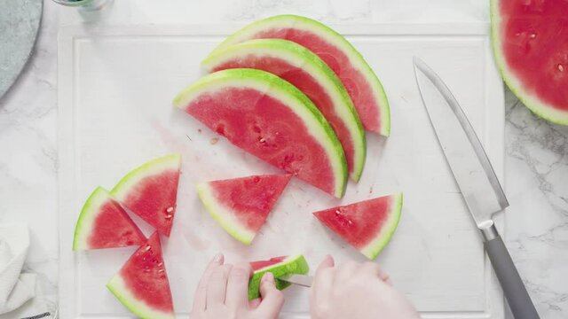 Time lapse. Flat lay. Slicing red watermelon into small pieces on a white cutting board.