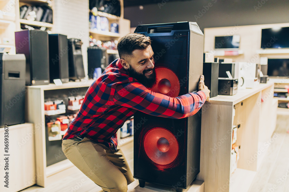 Wall mural Young man choosing music speaker for his home in an electronics store.