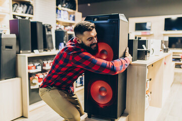Young man choosing music speaker for his home in an electronics store.