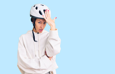 Beautiful brunette young woman wearing bike helmet and sporty clothes surprised with hand on head for mistake, remember error. forgot, bad memory concept.