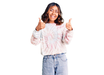 Young beautiful mixed race woman wearing casual tie dye sweatshirt success sign doing positive gesture with hand, thumbs up smiling and happy. cheerful expression and winner gesture.