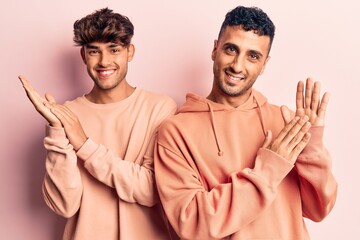 Young gay couple wearing casual clothes clapping and applauding happy and joyful, smiling proud hands together