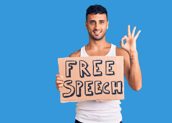 Young hispanic man holding free speech banner doing ok sign with fingers, smiling friendly gesturing excellent symbol