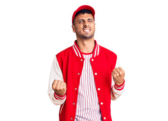 Young hispanic man wearing baseball uniform very happy and excited doing winner gesture with arms raised, smiling and screaming for success. celebration concept.