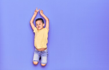 Adorable kid wearing casual clothes jumping over isolated purple background