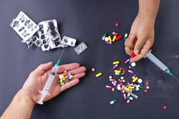 A concept with drugs, medicines, syringes and two hands showing the many drugs 