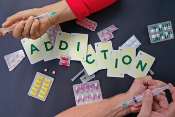 The word addiction written with cards and surrounded by drugs, medicines and syringes, a concept for addiction to medicines and drugs 