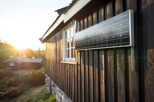 Solar panels hanging on cabin wall outdoors in the wilderness during sunset and warm light from sun hitting the panels. Sustainability, future and nature concept.