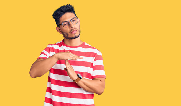 Handsome latin american young man wearing casual clothes and glasses doing time out gesture with hands, frustrated and serious face