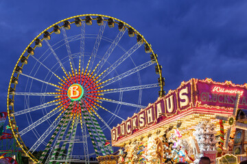 Night scenery atmosphere of colourful illuminated " GLUCKSHAUS " medieval gambling stall and background of Bellevue Ferris wheel, Rheinkirmes funfair festival.