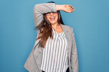 Young hispanic business woman wearing glasses standing over blue isolated background covering eyes with arm smiling cheerful and funny. Blind concept.