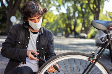 Man with face mask inflating the wheel of his bicycle on the street.