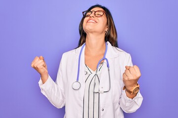 Professional doctor woman wearing stethoscope and medical coat over purple background excited for...