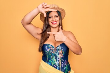 Young hispanic woman wearing summer hat and swimsuit over yellow background smiling making frame with hands and fingers with happy face. Creativity and photography concept.