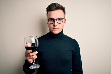 Young handsome caucasian man drinking an alcoholic glass of red wine over isolated background with a confident expression on smart face thinking serious